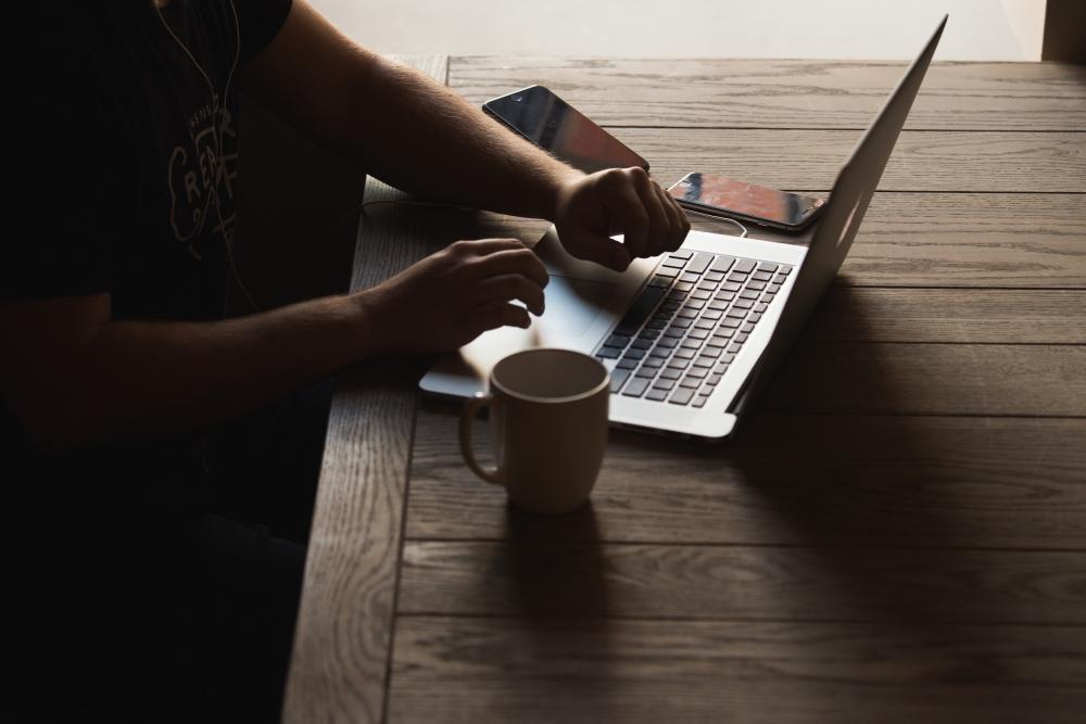 Manos en el teclado de un portátil junto a una taza de café, la pantalla está oculta