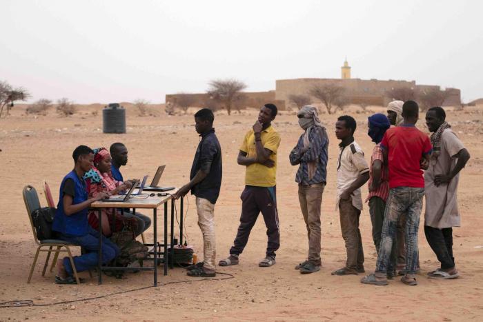 A group of young boys queueing in front of a desk with people and laptops