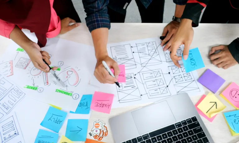 People planning an online resource on a desk with pens and paper