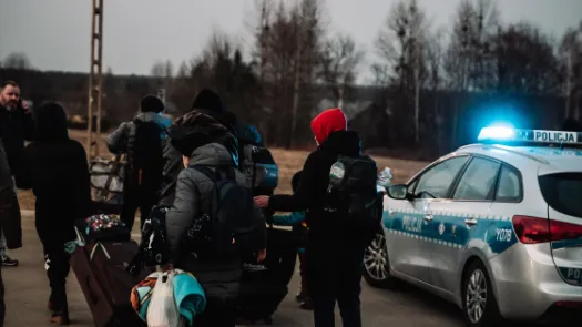 People with luggage and bags walking past a police car 