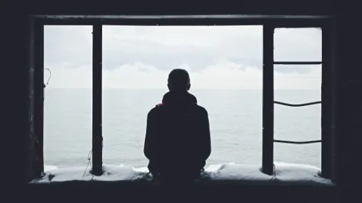 Man in silhouette sitting on a window ledge looking out to sea