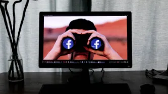 PC monitor showing individual with binoculars with Facebook image