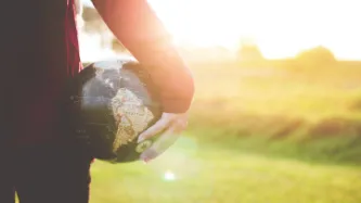 Person facing sunset holding a globe in hand