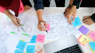 People planning an online resource on a desk with pens and paper